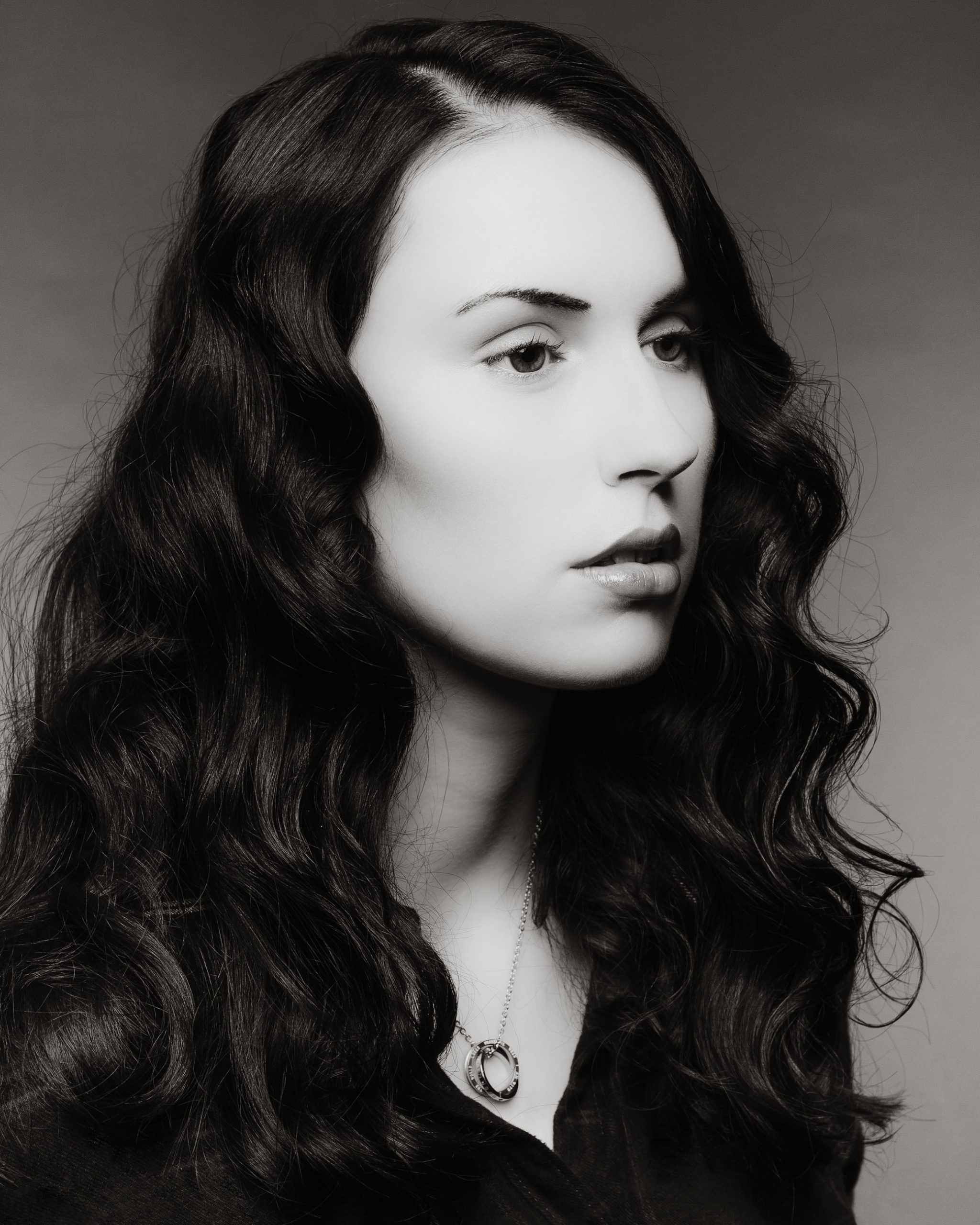 Frau mit dunklen lockigen Haaren vor grauem Hintergrund FOTOGRAF Sven Vogel Photograph Fotografie Schwarz Weiss Foto